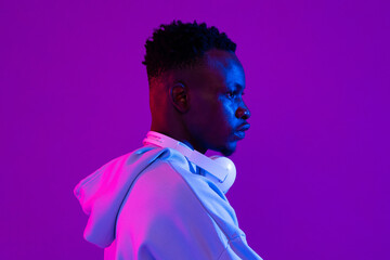 Side view portrait of young African man with headphones in neon light studio background