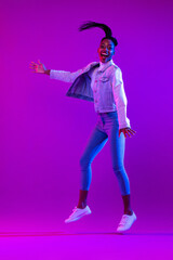 Obraz premium Full body portrait of ecstatic African-American woman jumping in modern neon light studio background
