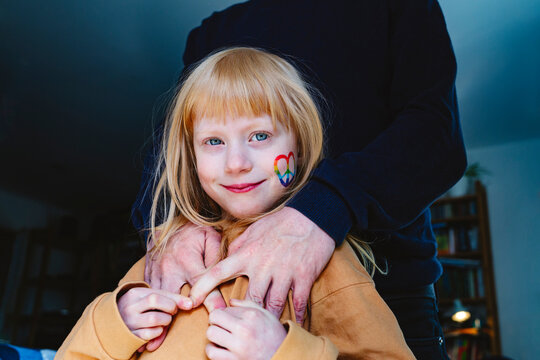 Smiling Blond Girl With Peace Sticker On Cheek Standing With Father At Home