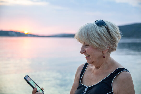 Smiling senior woman doing video call through smart phone by sea on sunset
