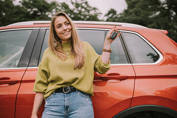 Smiling young woman with key standing in front of car
