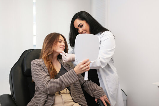 Dermatologist examining patient looking in mirror after botox treatment at aesthetic clinic