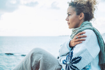 Thoughtful woman in warm clothing hugging self by sea
