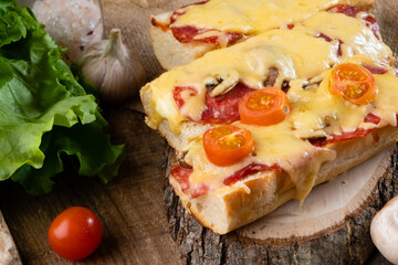 Italian baked sandwich. Pizza on a baguette baked with cheese and pepperoni sausages, and cherry tomatoes on a wooden table.