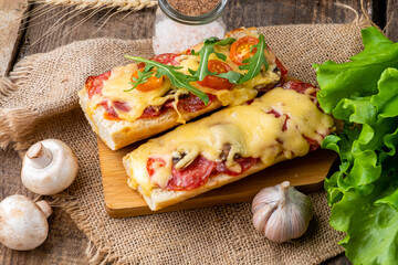 Pizza sandwich cooked on a baguette with cheese, sausages and herbs, arugula. Wooden background.