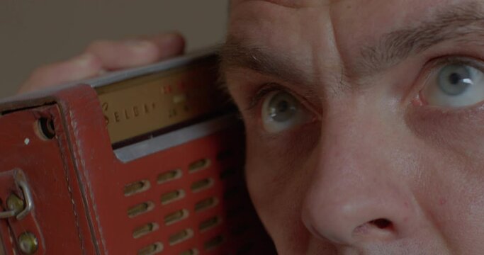 A man listens to the radio speaker in his hands. He listens to a faint sound signal. Analogue broadcasting of information. Close-up of the eye. Soft focus. CZ, Kladno, Armenska, 6.2.22.
