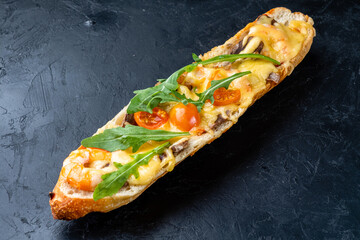 Pizza sandwich. Pizza cooked on a baguette with cheese, tomatoes, shrimps and arugula on a dark table.