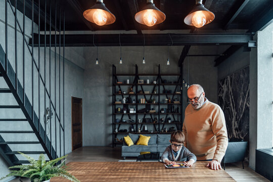 Boy turning pendant lights on through tablet PC sitting by grandfather at home