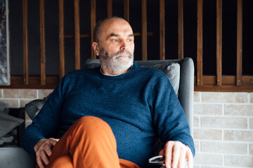 Thoughtful senior man sitting on armchair at home