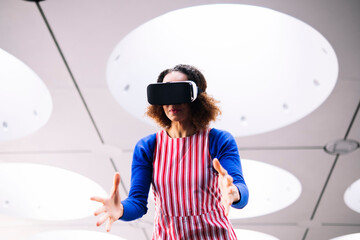 Mature woman wearing VR goggles gesturing under illuminated ceiling