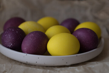 Bright and beautiful Easter eggs, purple and yellow, on a white plate. Christ is risen. Happy Easter.
