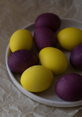 Bright and beautiful Easter eggs, purple and yellow, on a white plate. Christ is risen. Happy Easter.