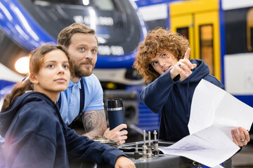 Engineer holding blueprint explaining to trainees at industry