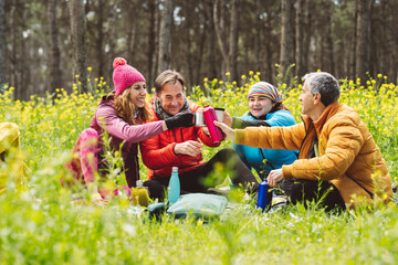 Smiling men and women toasting bottles and cups sitting in forest