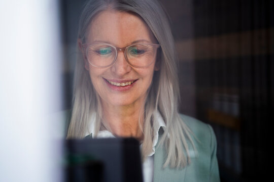 Smiling businesswoman with tablet PC seen through glass