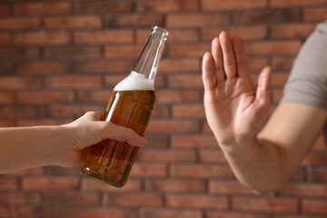 Man refusing to drink beer near red brick wall, closeup. Alcohol addiction treatment