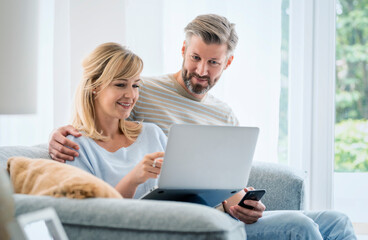 Happy woman and man relaxing on the sofa at home while using laptop and mobile phone