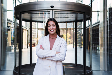 Smiling businesswoman with arms crossed standing in front of revolving door