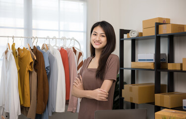 Happy Young beautiful asian woman business owner at fashion store check stock on rails clothing standing and smile. Asian female entrepreneur working in clothes shop.