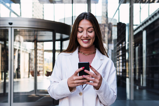 Happy businesswoman using mobile phone at office building