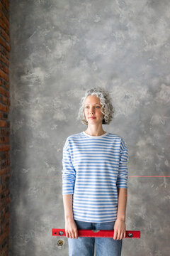 Woman with level measuring tool standing in front of gray wall