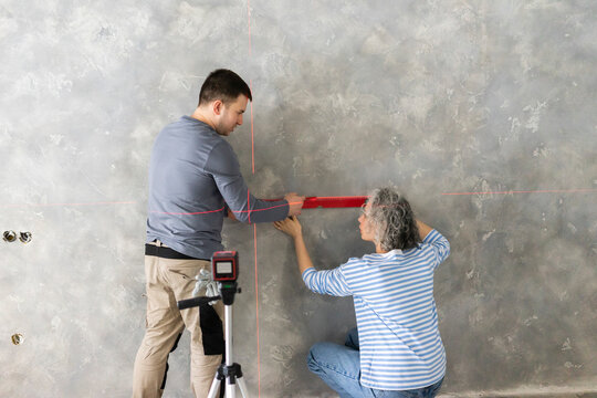 Woman and friend measuring construction laser level on gray wall