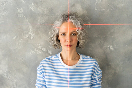 Woman with laser level on face in front of gray wall