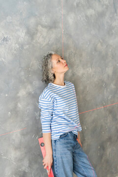 Tired thoughtful woman holding level leaning on gray wall
