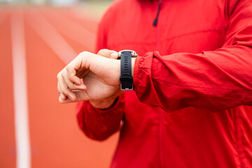 Young man wearing sportswear red jacket using Smart Watch Showing Heart Rate Monitor. Technology for health and sport mode. Exercise and take statistics to develop your potential.