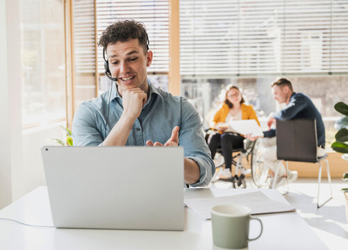 Young man with headset and laptop at desk in office