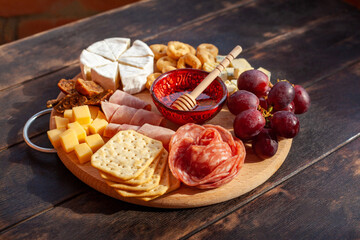 Round cutting board with slicing assorted cheese, sausage rosette, ham, cracker, grapes and figs with honey - Powered by Adobe
