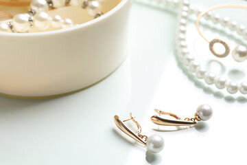 Elegant golden earrings and other stylish jewelry with pearls on white table