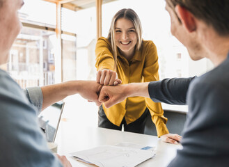 Happy business team touching fists in office