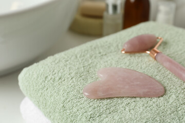 Rose quartz gua sha tool and natural face roller on towel in bathroom, closeup