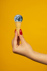 Woman hand holding small crispy ice cream cone with a mirrored disco ball isolated on yellow...