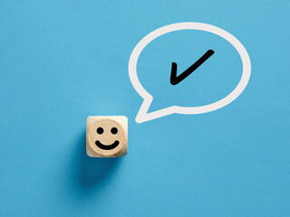 Happy face icon on a wooden cube with tick check mark or checkmark symbol in a speech bubble.