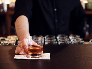 Male bartender serves a glass of neat whiskey at the pub