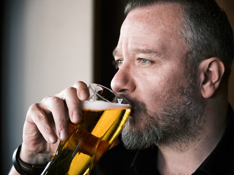 Close up portrait of a hipster man in his 40s drinking a glass of beer in a bar or pub.