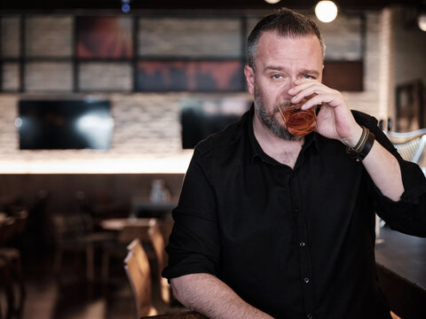 Portrait Of A Handsome Mature Man Drinking A Glass Of Neat Whiskey At The Bar Or Pub.