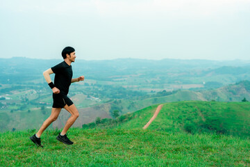 Portrait of an Asian male trail runner running. On the high mountains there are beautiful views. It's a trail running practice. on a bright day Behind is a beautiful mountain view.