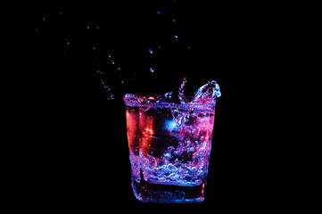 Splash of water in rocks glass with beautiful pink and blue bubbles isolated on black background