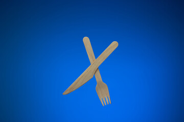 Naklejka na ściany i meble Single use disposable and biodegradable wooden knife and fork. Close up studio shot, isolated on blue background