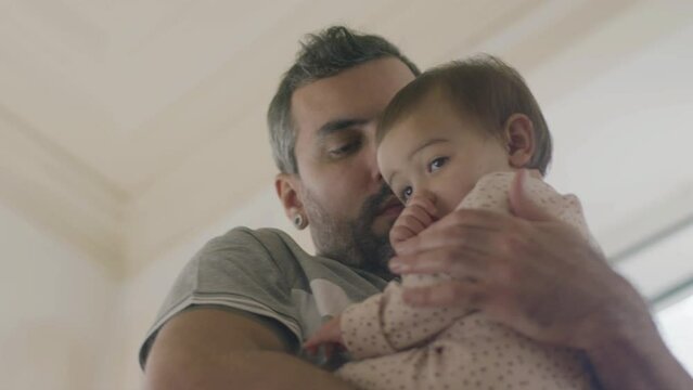 Handsome young man cradling cute baby girl in his arms. Caring father standing and holding infant daughter in his arms, swaying from side to side. Parenthood, fatherhood concept