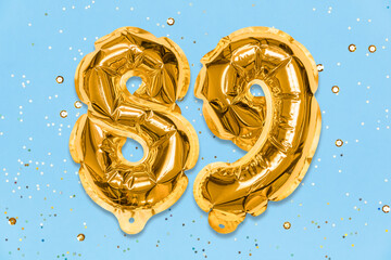 The number of the balloon made of golden foil, the number eighty-nine on a blue background with sequins. Birthday greeting card with inscription 89. Numerical digit. Celebration event, template