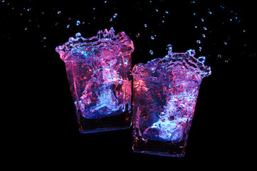 Two rocks glasses clinking with big splash on a black background, close-up