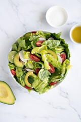 Avocado salad with lettuce and vegetables on a marble background, top view.