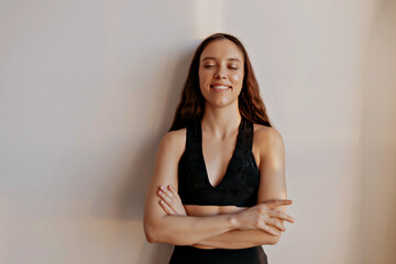 Wonderful stylish european woman in black sport top is holding arms on the chest and smiling with closed eyes over isolated background 