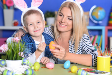 Son and mother painting traditional Easter eggs in different colors at home, with pleasure preparing to religious spring holiday