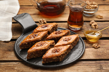 Delicious sweet baklava with walnuts, honey and hot tea on wooden table