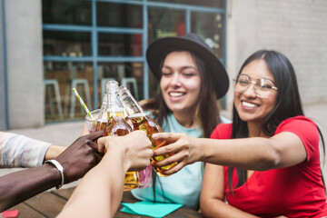 Two girls young friends having drinks together toasting beer and cocktail to celebrate social event. Focus on latin woman
